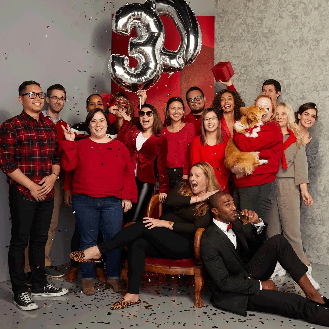 The finished K&G campaign image: a team in red around silver 30 balloons, with confetti and a corgi