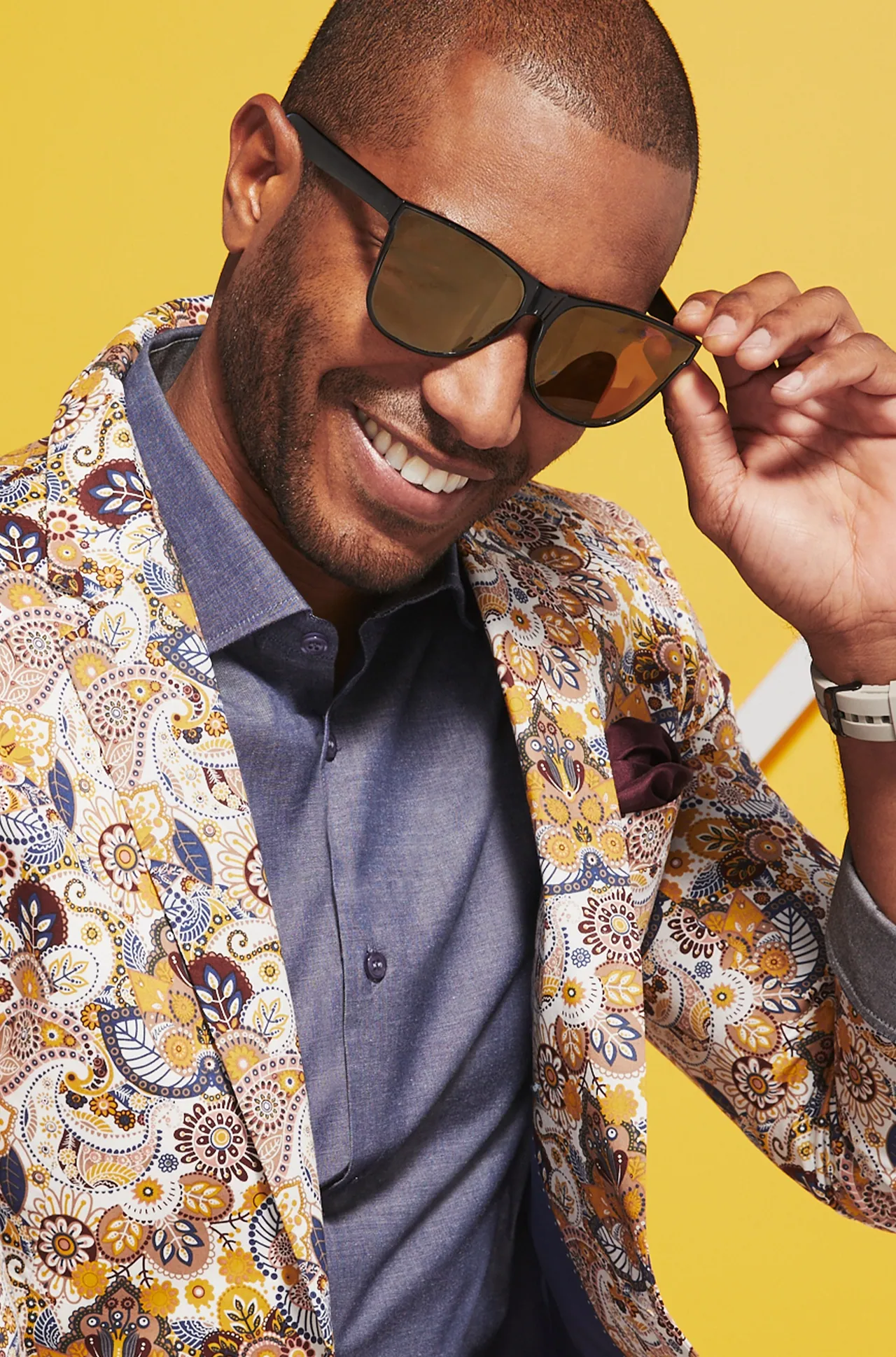 Model in a paisley jacket and sunglasses on a yellow set