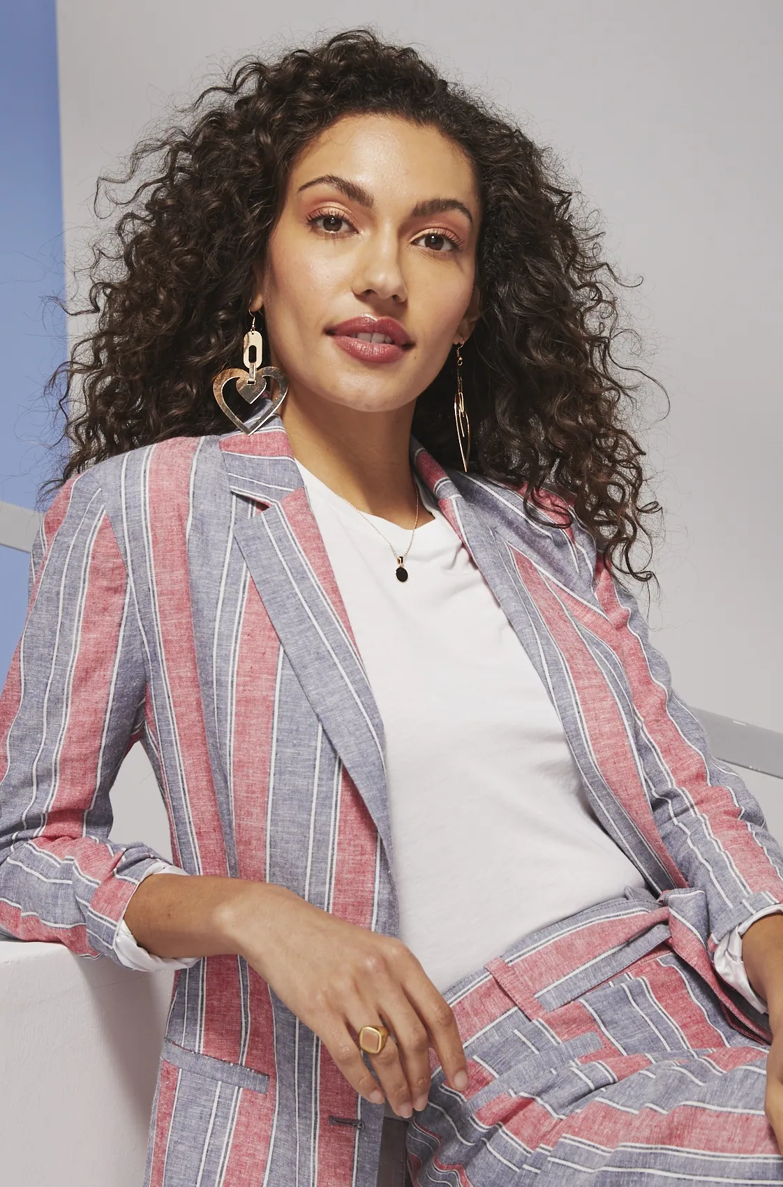 Model in a coral and blue striped suit seated on a white block