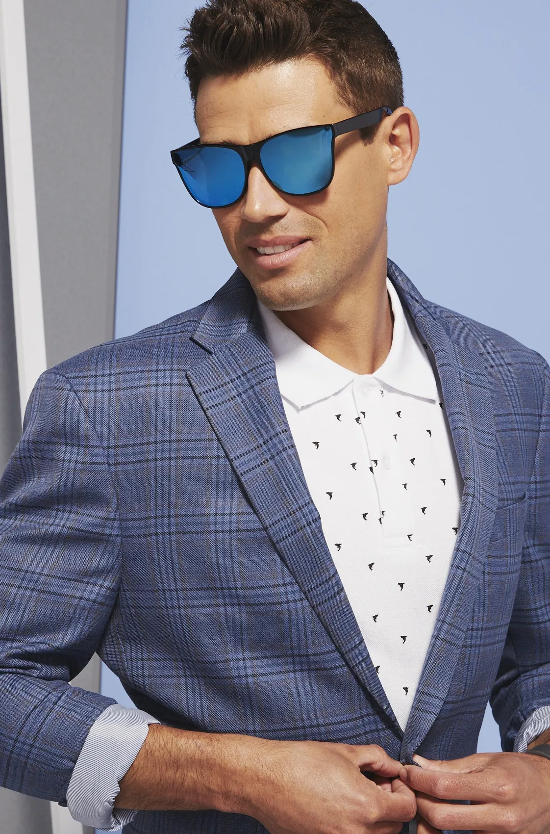 Model in blue sunglasses and a plaid blazer against gray and blue walls