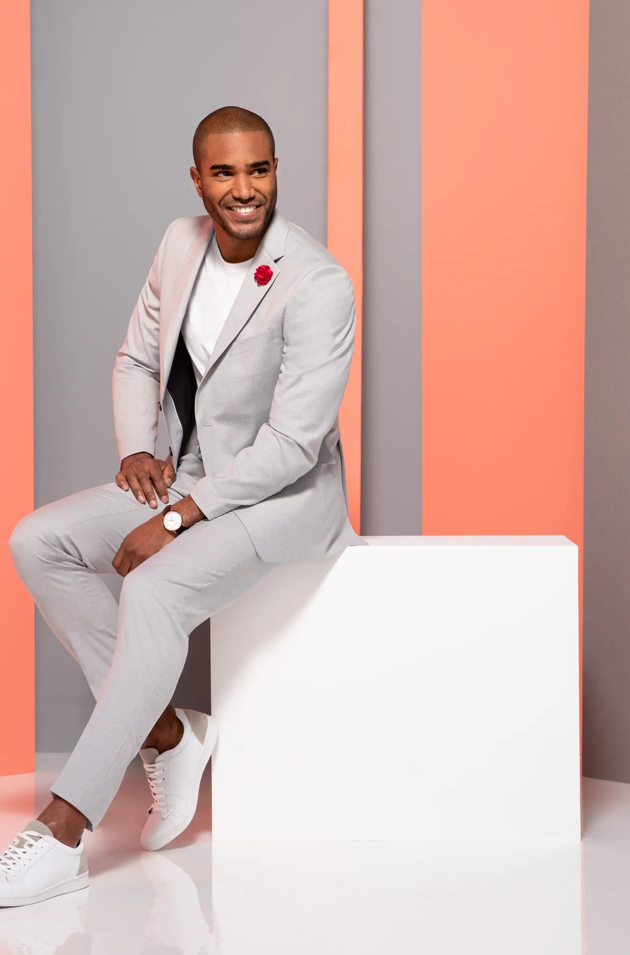 Model in a white suit holding a hat on a coral set
