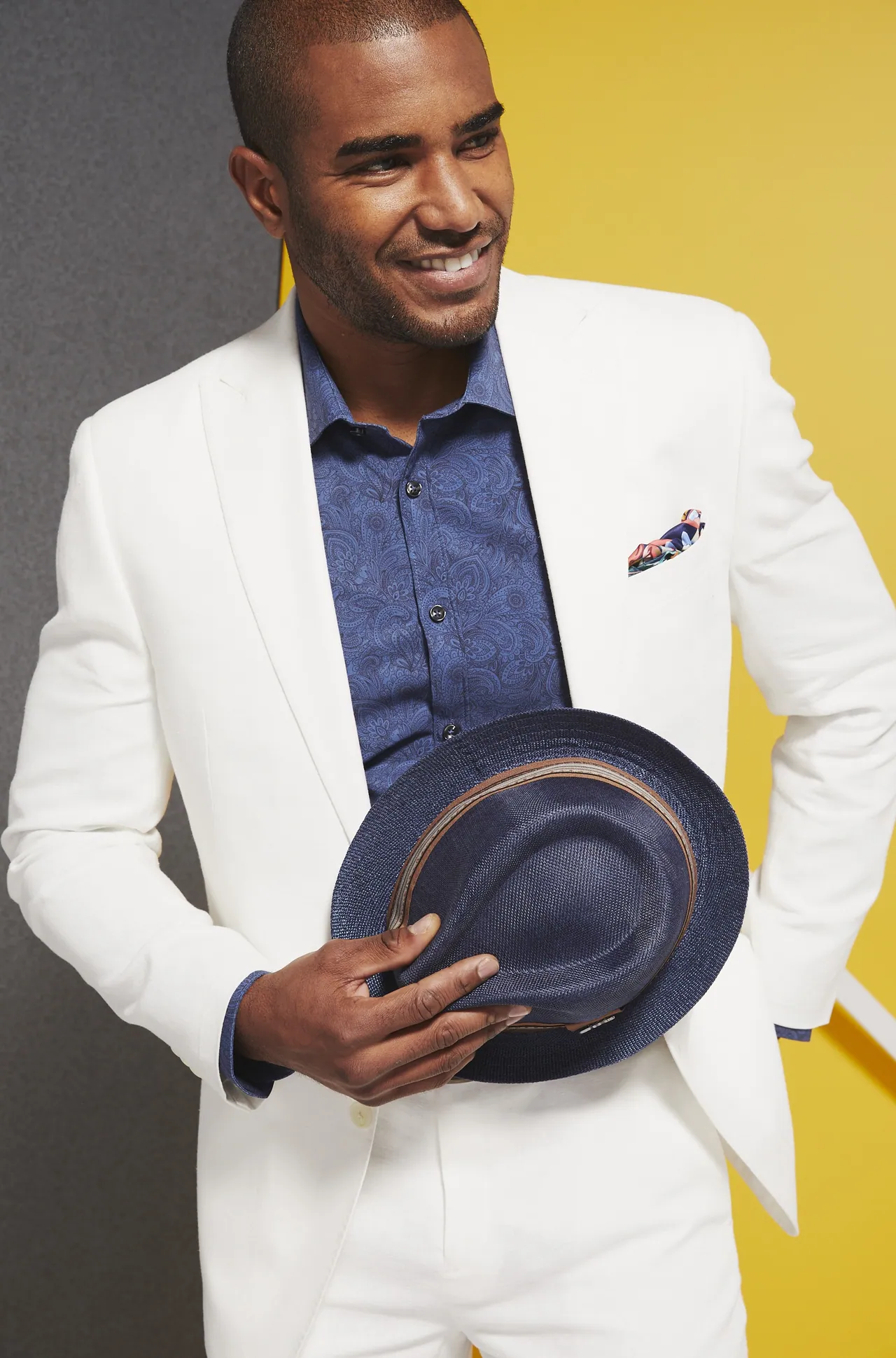 Model in a white suit and patterned shirt on a yellow set