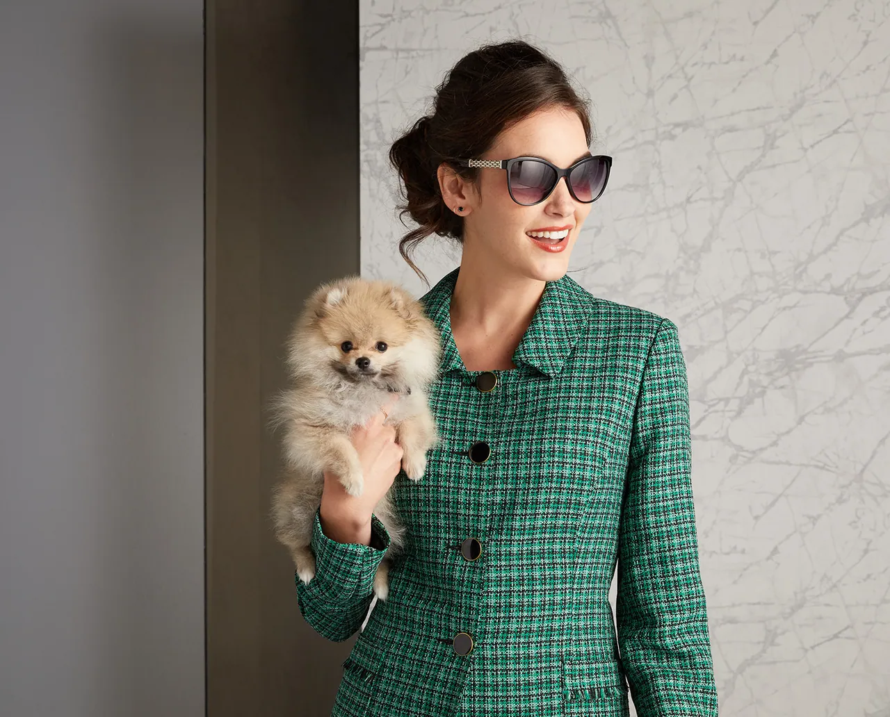 Model in a green checked coat holding a small dog
