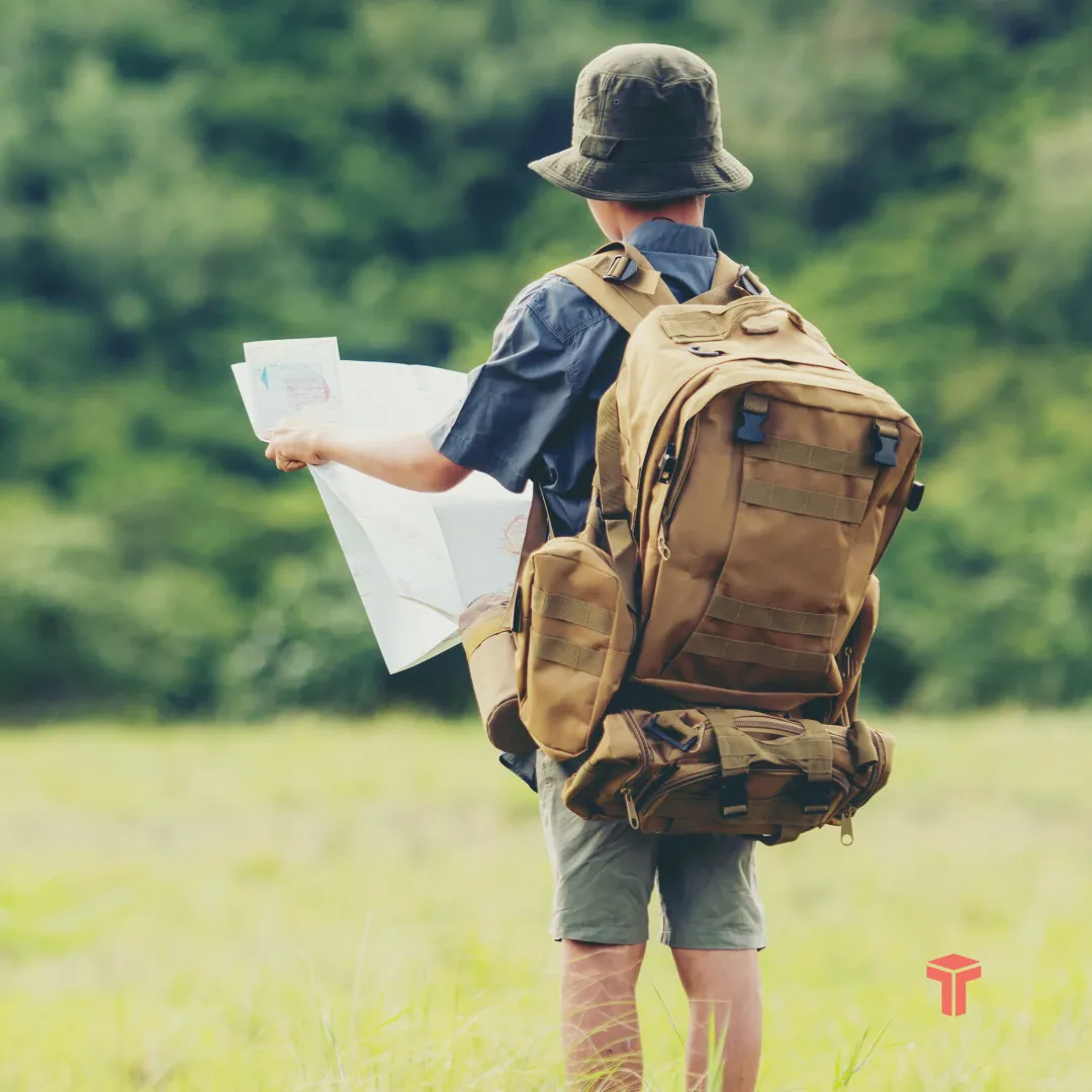 Carousel slide two: a boy with a map and backpack in a meadow