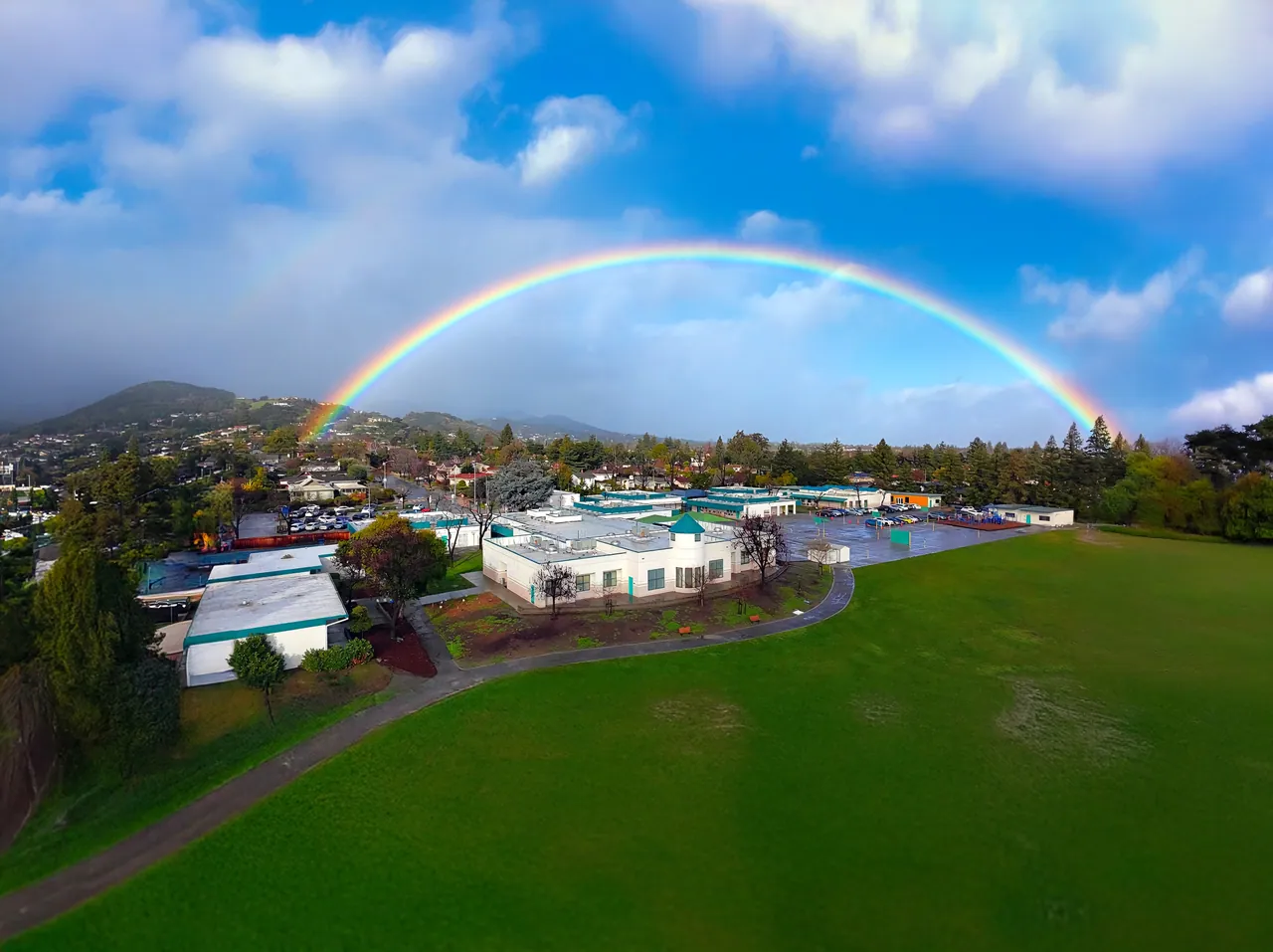 An aerial view of the Tessellations campus under a full rainbow, with four pages from the 2025 brand guidelines on the right