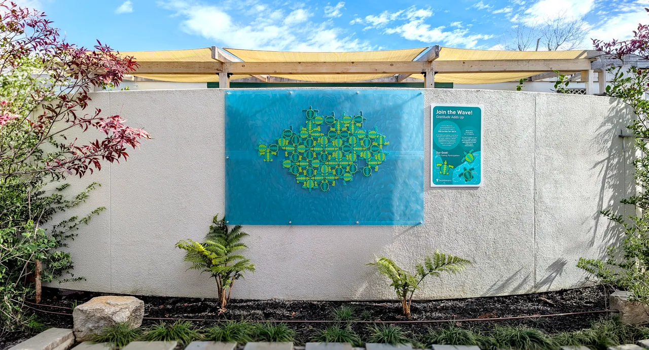 The installed mural: a field of green and teal turtles fitted together on a translucent blue panel, with the Join the Wave sign beside it