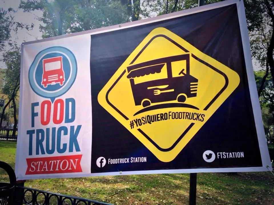 A banner on a railing with the Food Truck Station logo and a yellow road-sign badge reading #YoSíQuieroFoodtrucks